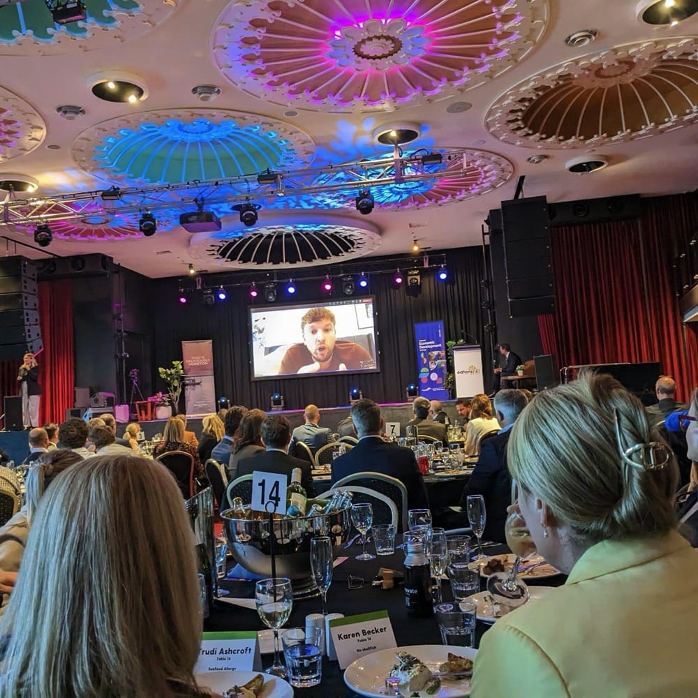 People around tables having dinner in large hall. They are also watching a video on a large projected screen. Live event audio Brisbane, Gold Coast, Sunshine Coast