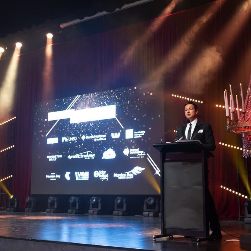 Man stands behind lecture at awards ceremony. Live event audio Brisbane, Gold Coast, Sunshine Coast