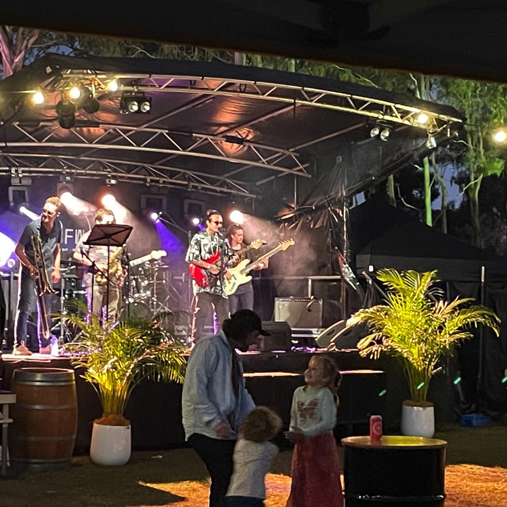 Band plays on outdoor stage. A father with two young children dance in front. Live event audio Brisbane, Gold Coast, Sunshine Coast