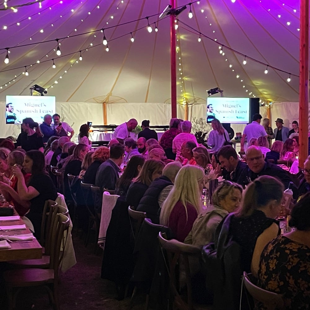 Dinner Event. People sitting around long table eating. They are in a tent with lights above.Live event audio Brisbane, Gold Coast, Sunshine Coast