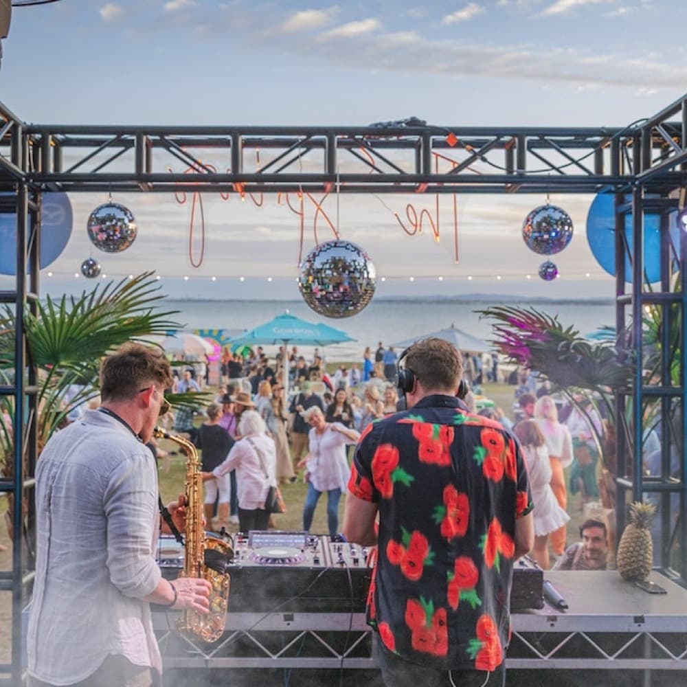 DJ in front of dancing people with saxophone player. A mirror ball hangs from truss. Live event audio Brisbane, Gold Coast, Sunshine Coast